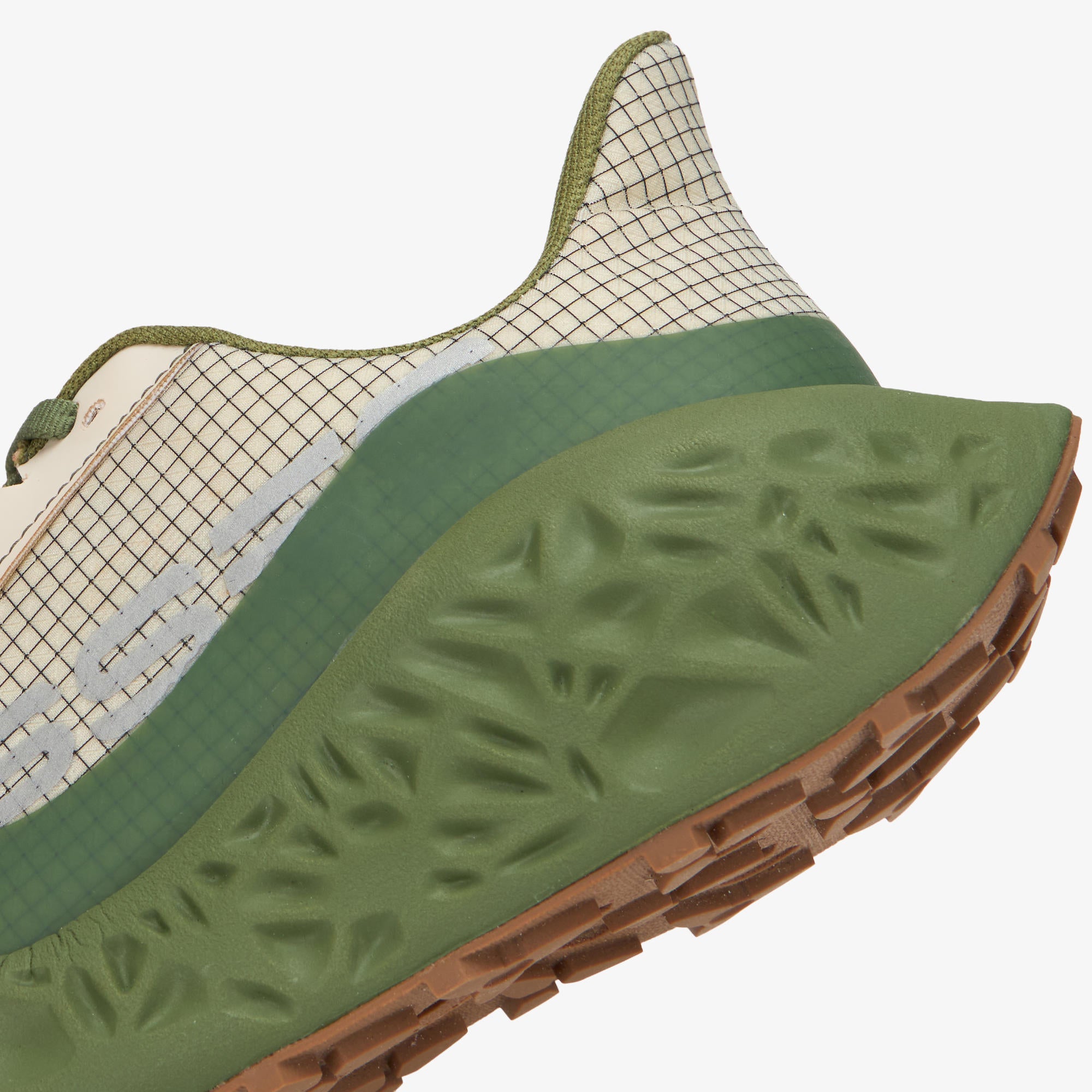 Close-up of a trail running shoe showing the textured olive green midsole, brown outsole, and off-white mesh upper on a light gray background.