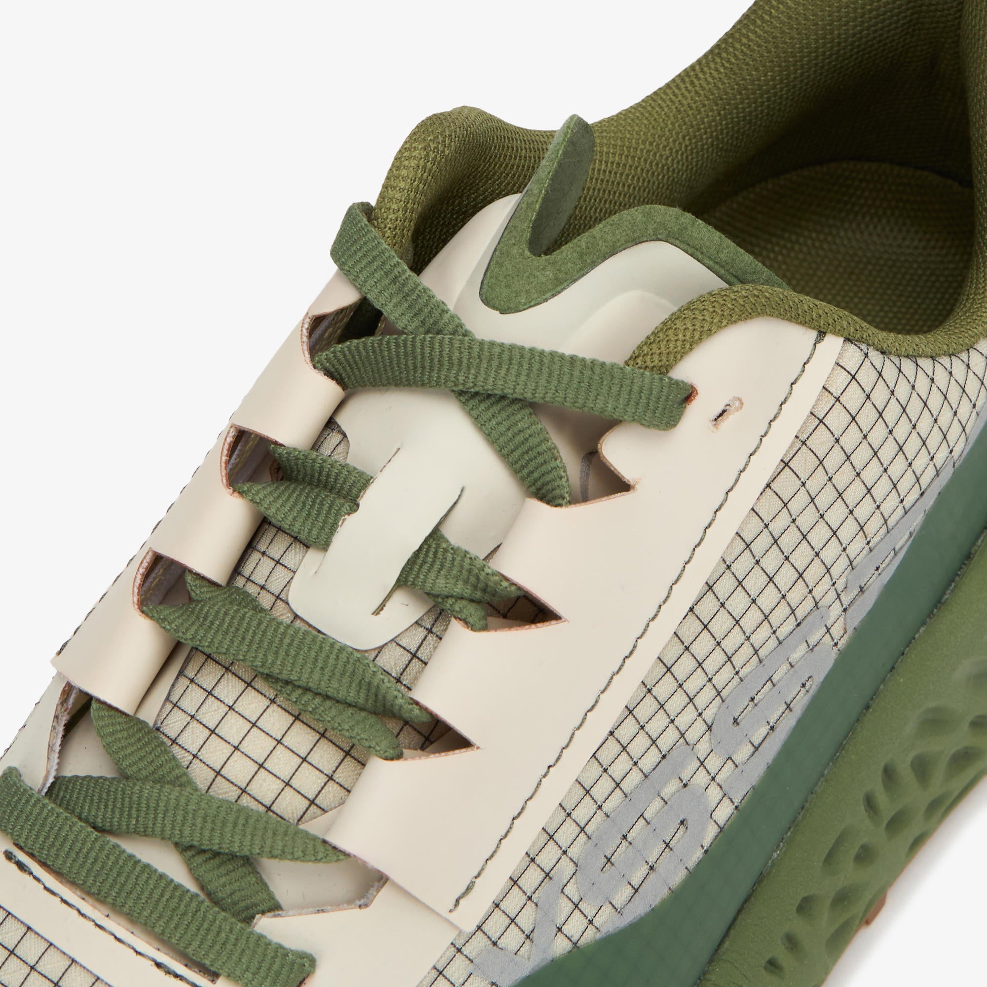 Close-up of a low-top ULYSSES MAIKOH showing the side panel, laces, tongue, and part of the sole in muted olive green and off-white tones.