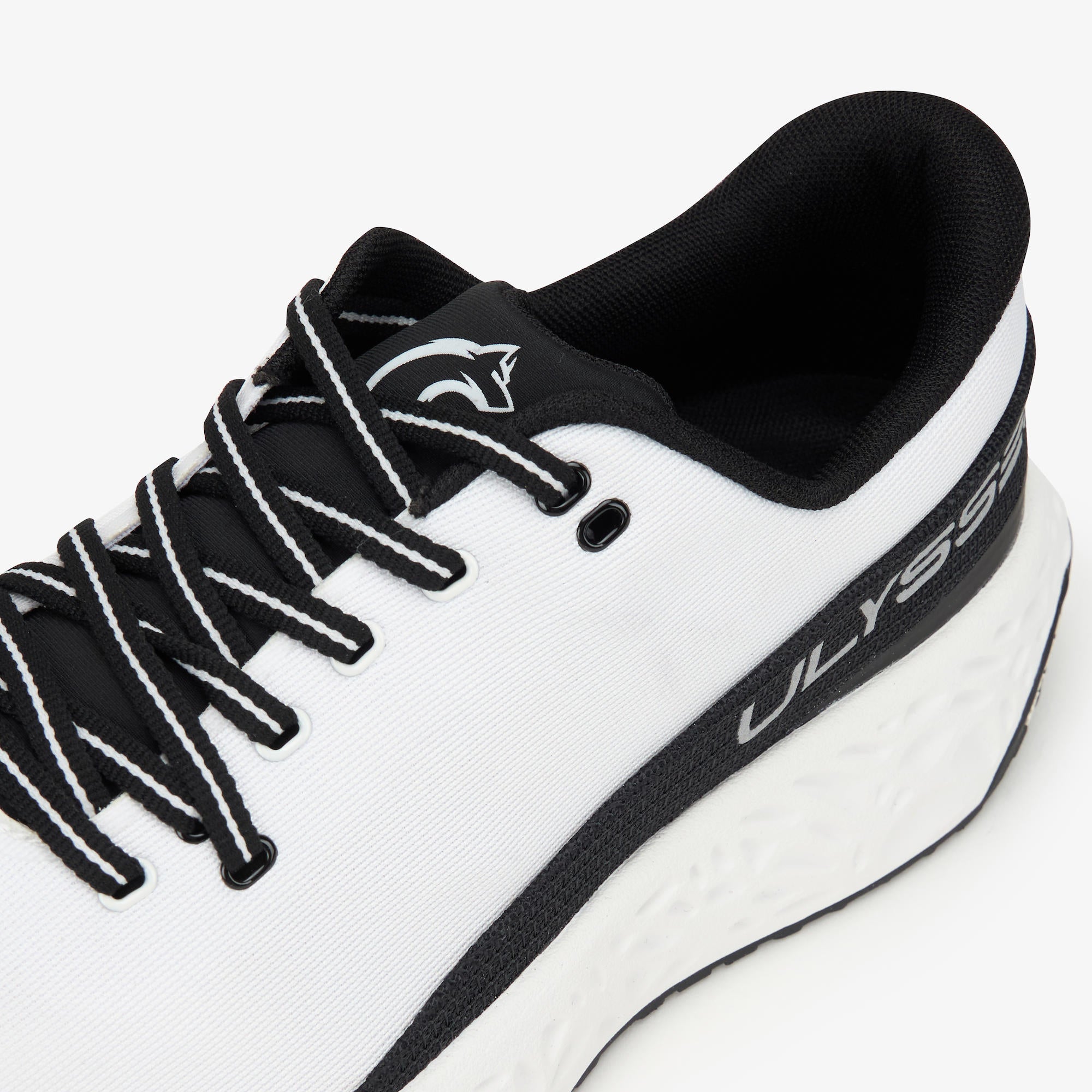 Close-up of a white and black Ulysses athletic shoe showing the side profile, black laces with white stripes, and the Ulysses branding on the heel.