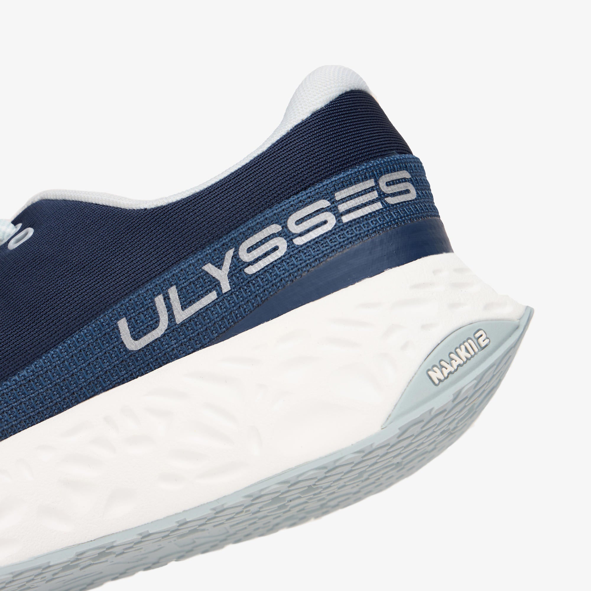 Close-up of a running shoe showing the navy blue Ulysses heel collar, white midsole, and light gray outsole with NAAKII II branding on a clean white background.