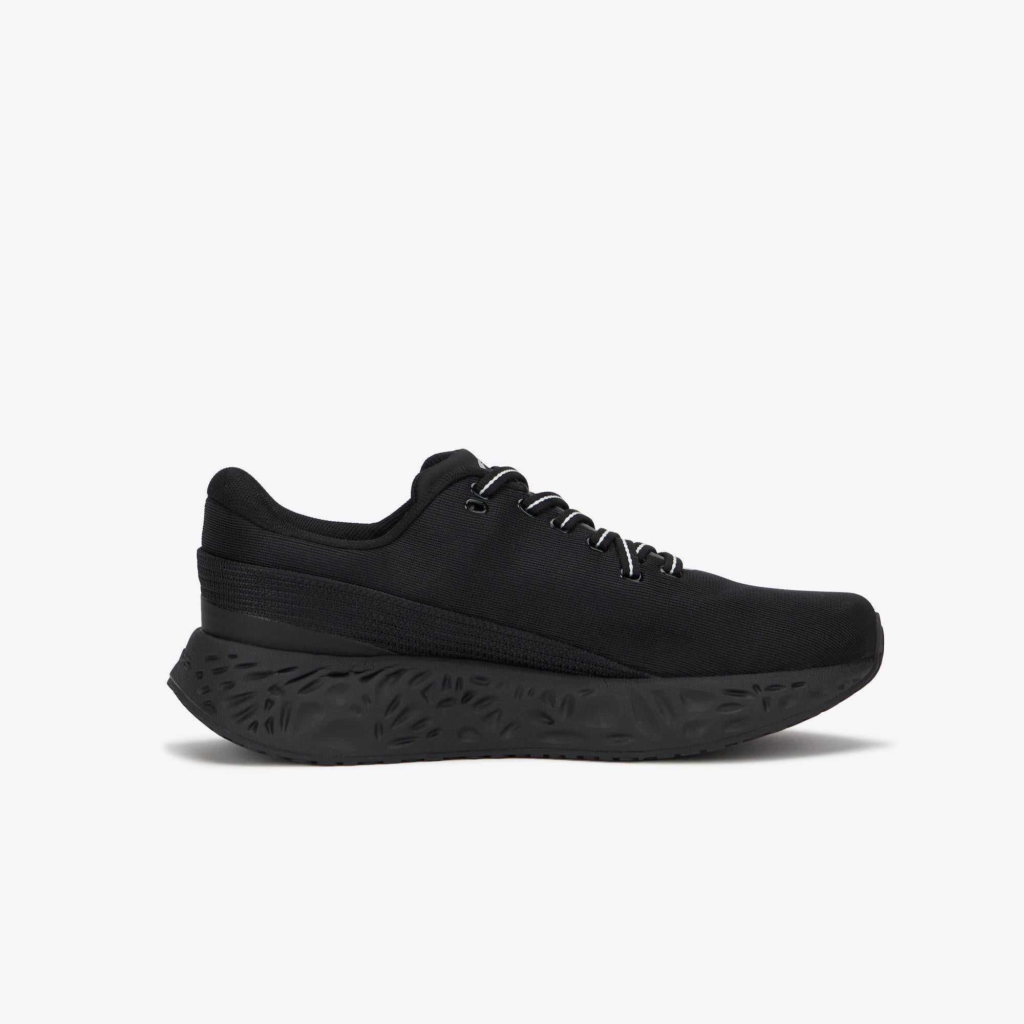 A black low-top athletic sneaker with a thick, sculpted black sole and white laces, shown in a side profile on a light gray background.
