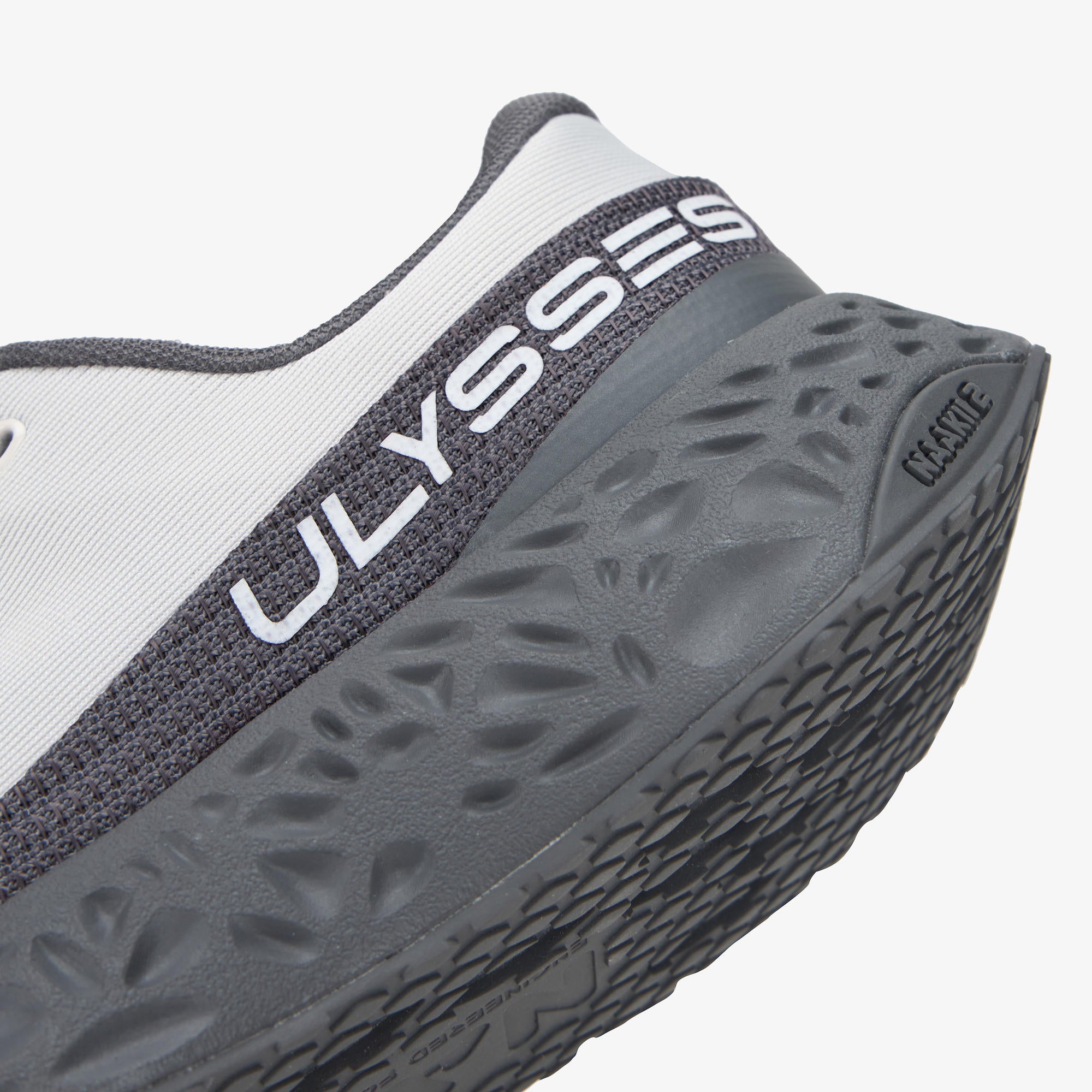 Close-up of a running shoe showing the heel area with a white upper, dark gray mesh band, and textured dark gray sole