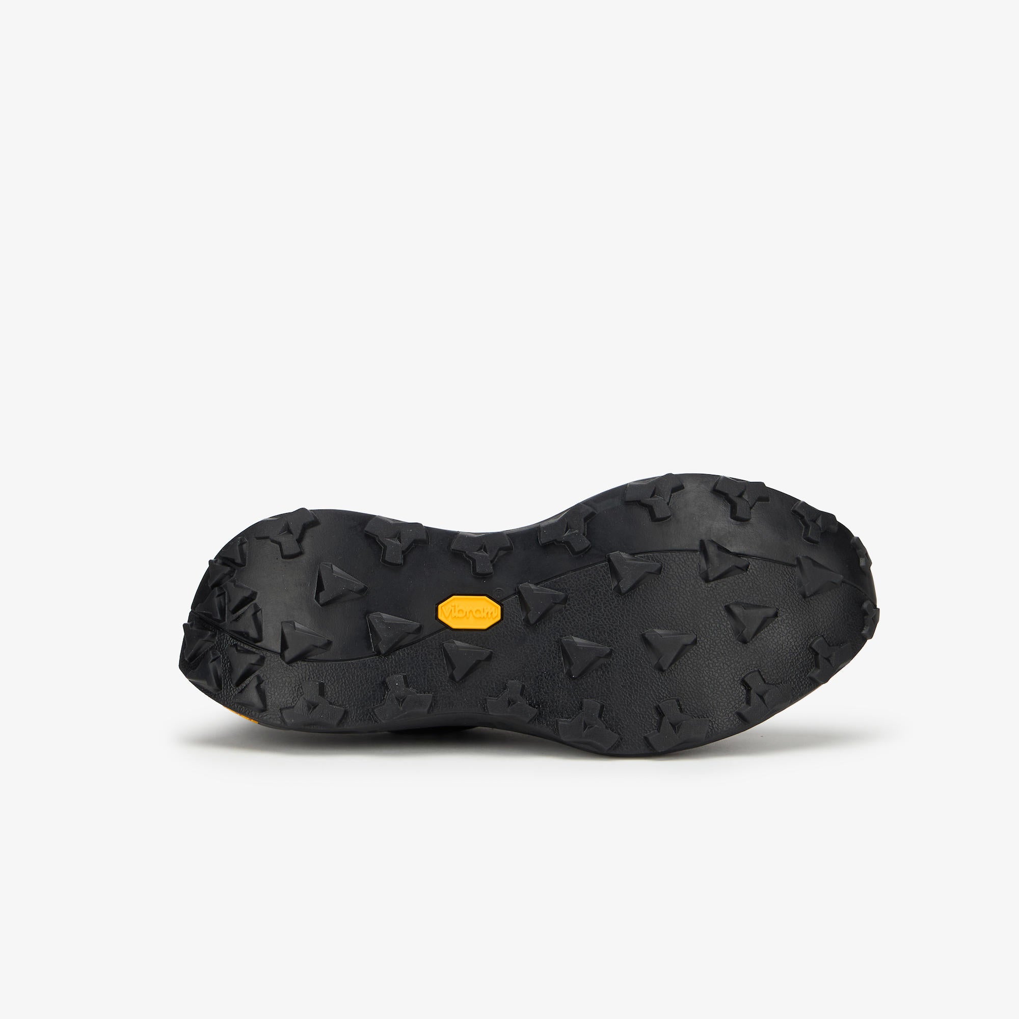 The black rubber outsole of a shoe, featuring a textured tread pattern and a small yellow Vibram logo in the center, shown against a light gray background.