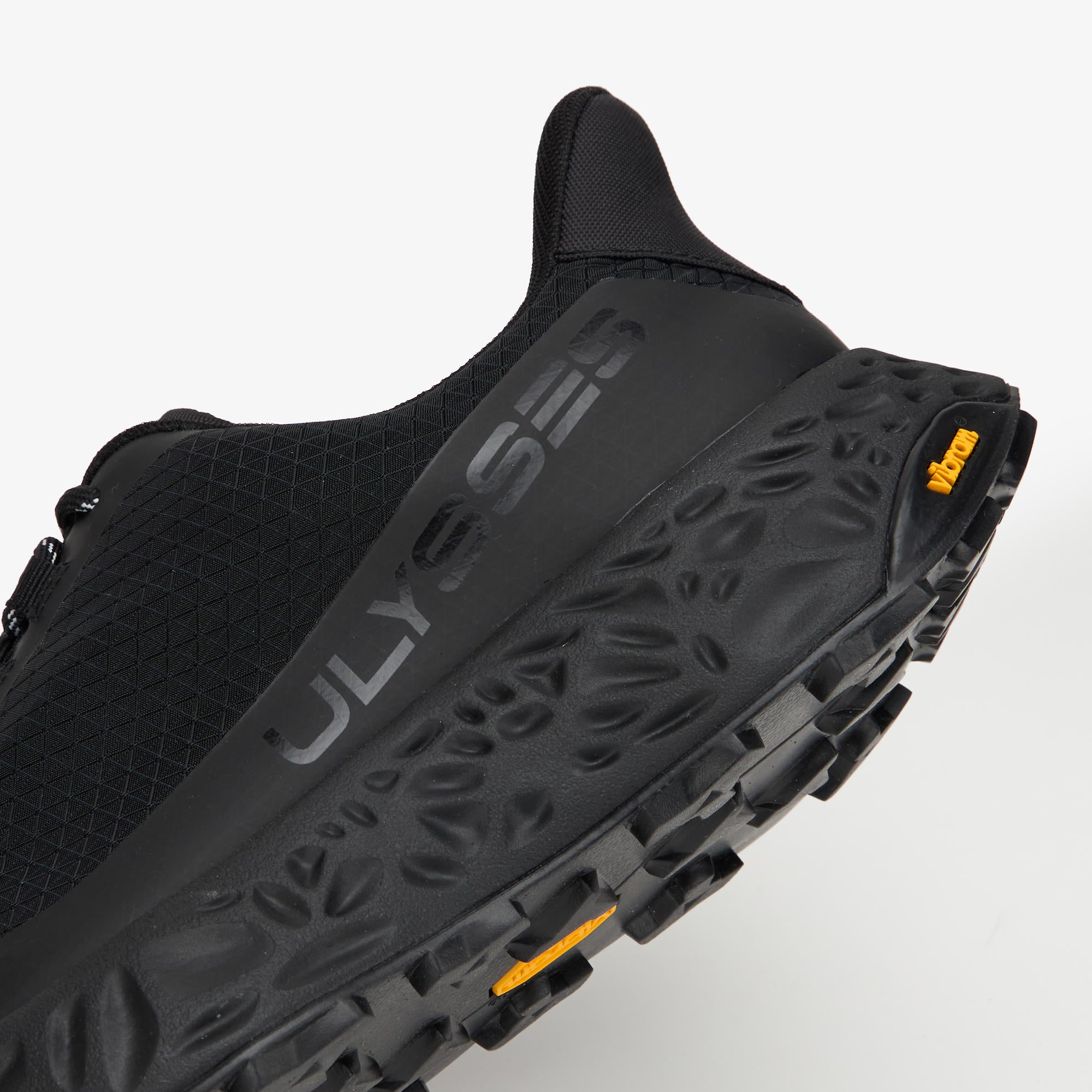 Close-up of a black Ulysses trail running shoe showing the textured midsole, side branding, and a small yellow Vibram logo on a light gray background.