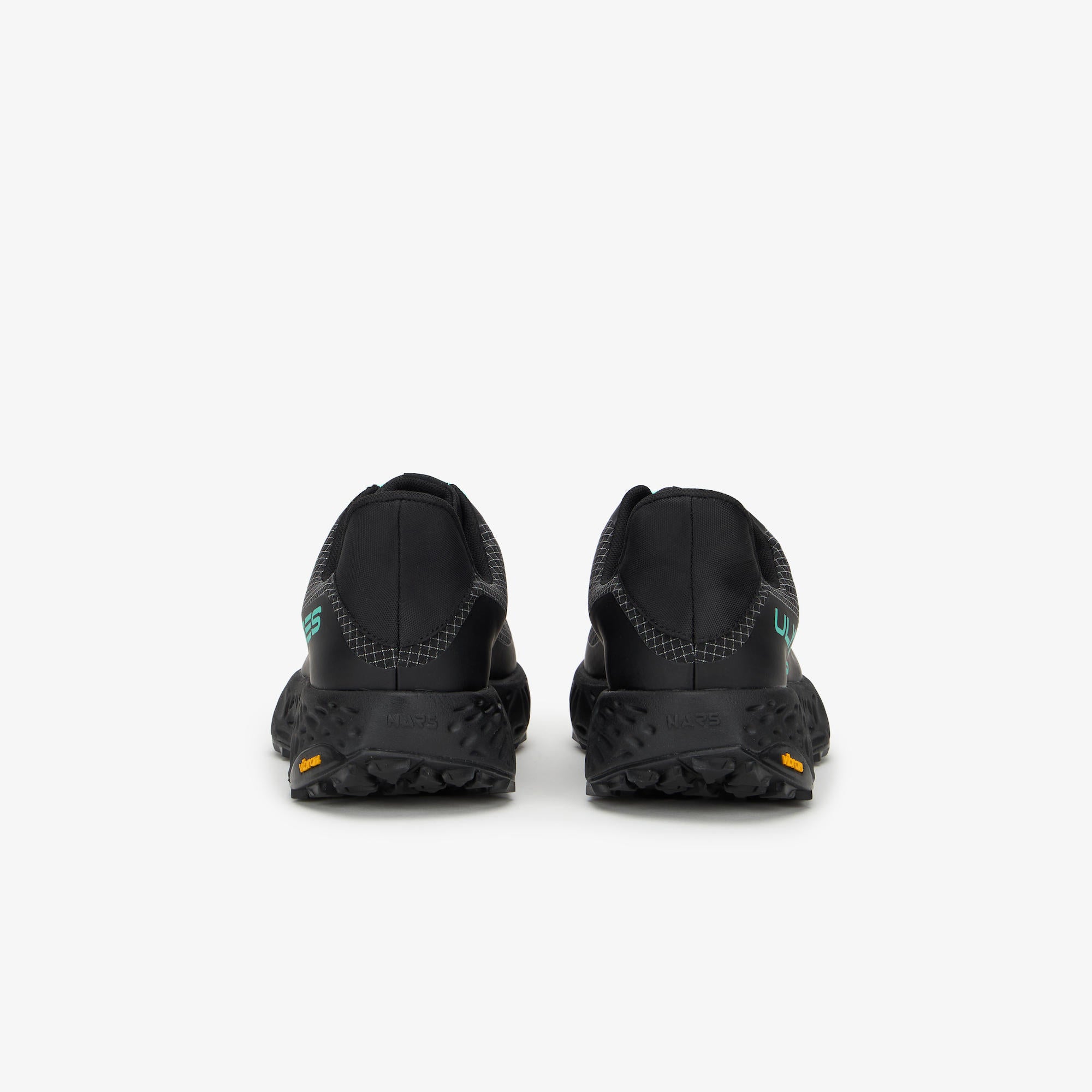 Black trail running shoes shown from the rear, featuring textured black midsoles and small green and orange accents near the heel, set against a plain white background.