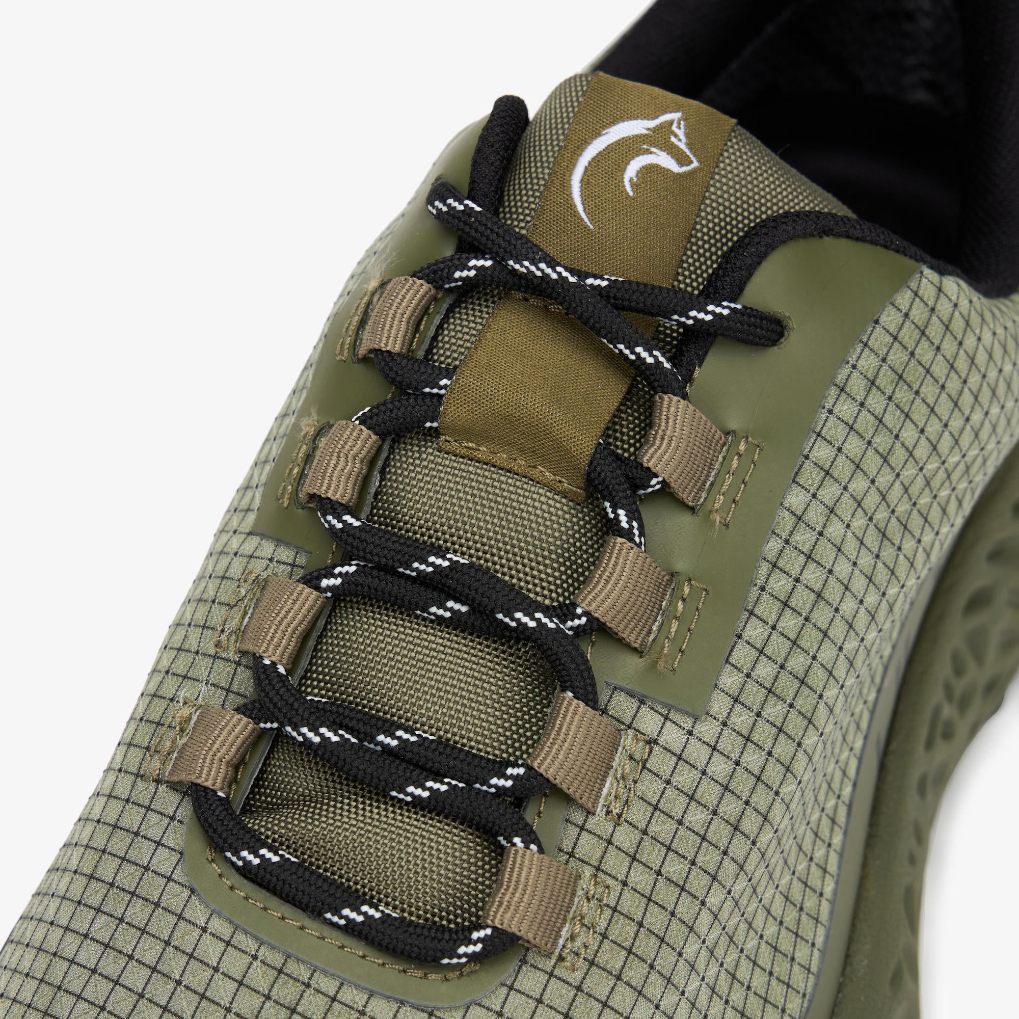 Close-up of a green and beige grid-patterned ULYSSES NANUK with black and white patterned laces and a tan tongue patch featuring a white fish logo.