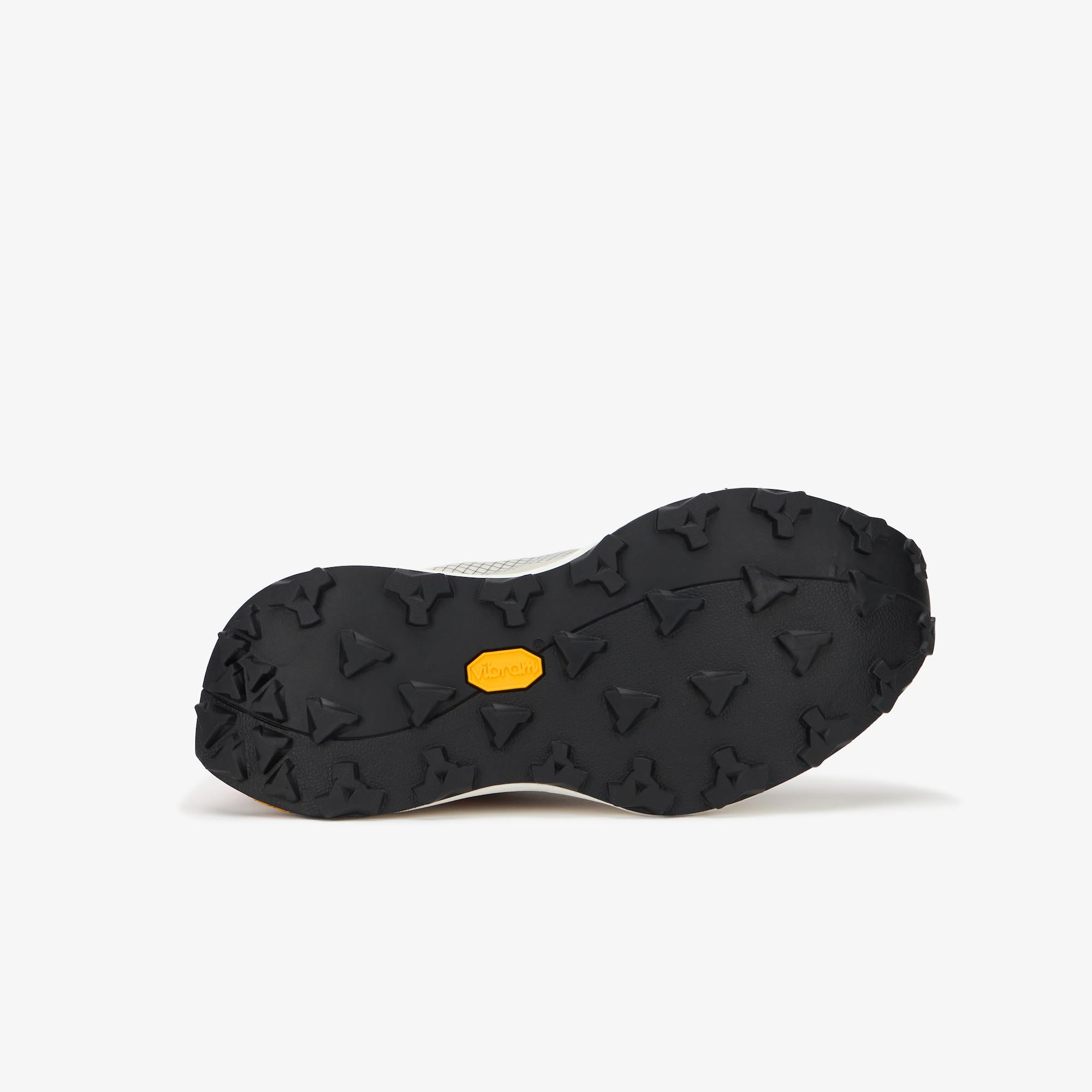 The outsole of a black athletic shoe, showing deep tread patterns and a small yellow Vibram logo in the center, photographed on a light gray background.