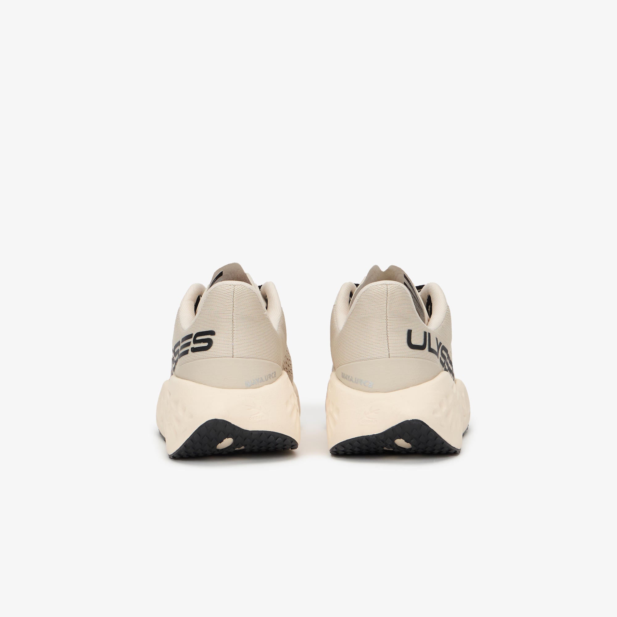 A pair of beige and off-white running shoes shown from the back, featuring black branding text on the heel and a black outsole, set against a plain light gray background.