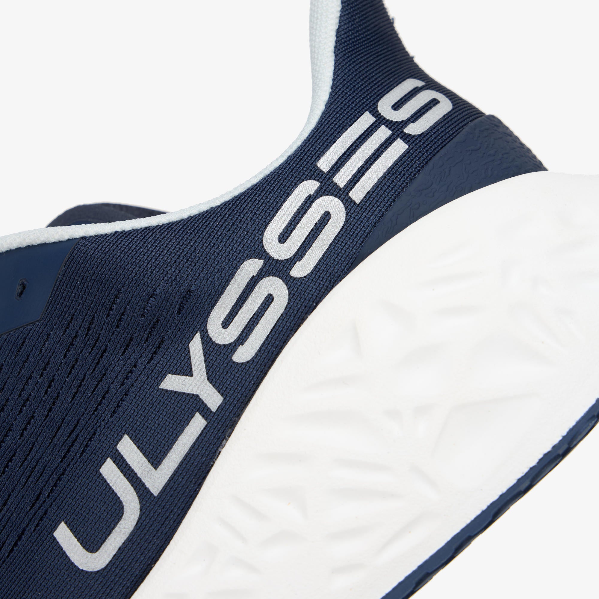 Close-up of a Waya navy blue and white running shoe showing the side profile with the ULYSSES branding on the heel collar and a textured white midsole.