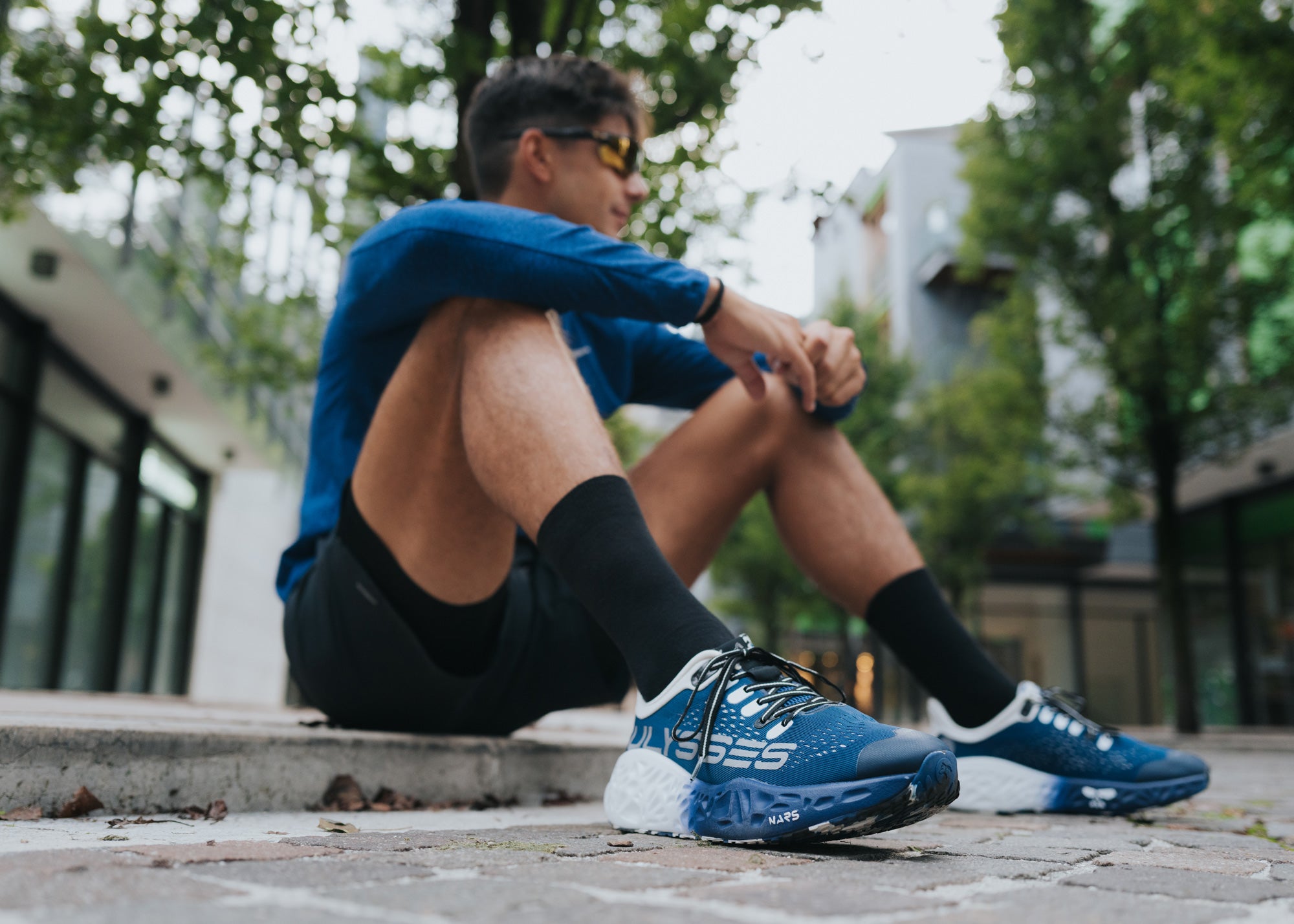 A runner sitting on outdoor steps wearing blue Ulysses running shoes, showcasing the shoe’s grip on an urban surface.