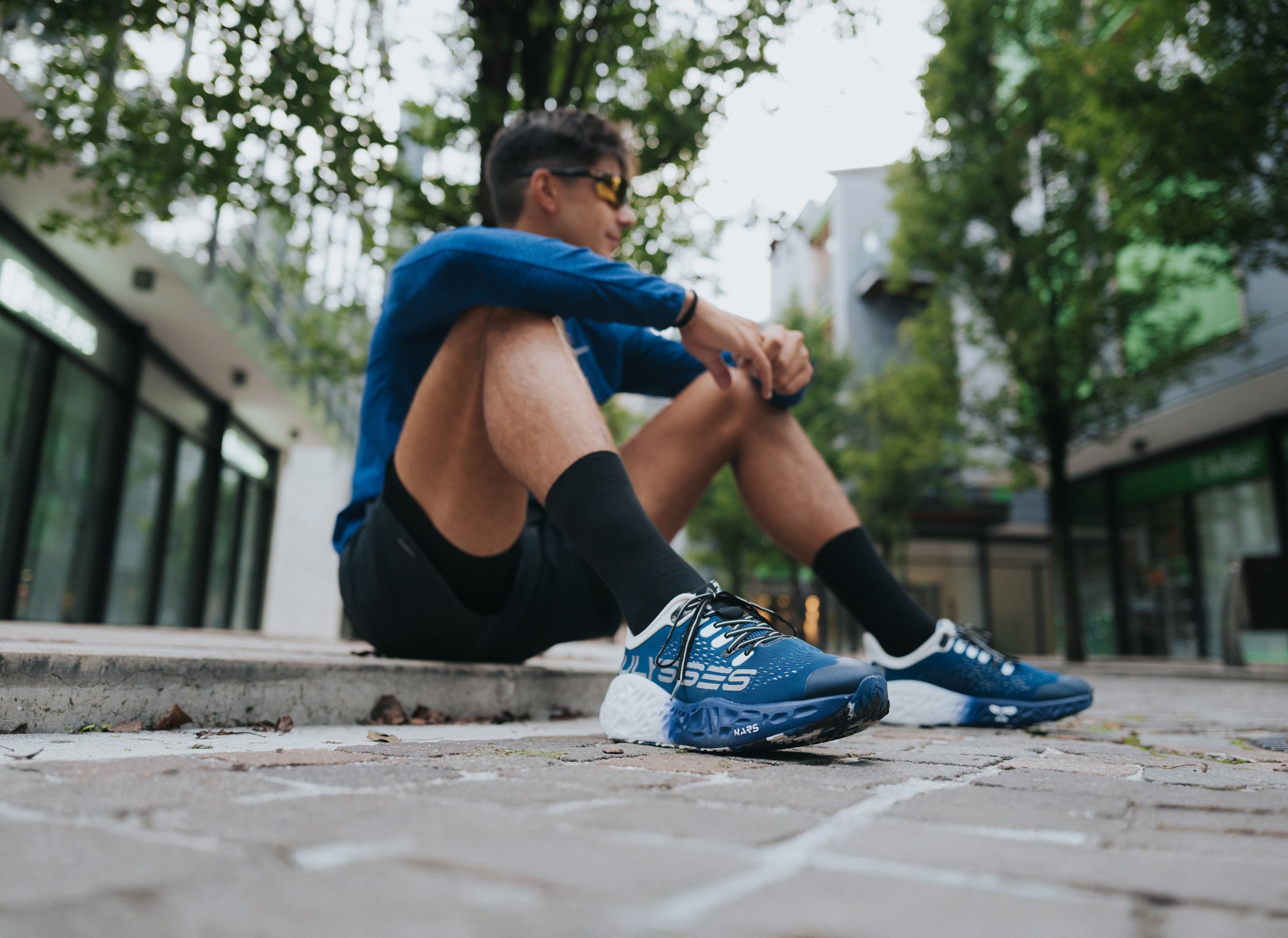 Runner sitting in an urban setting wearing Ulysses Waya on road running shoes, a blue model designed for asphalt and city running.