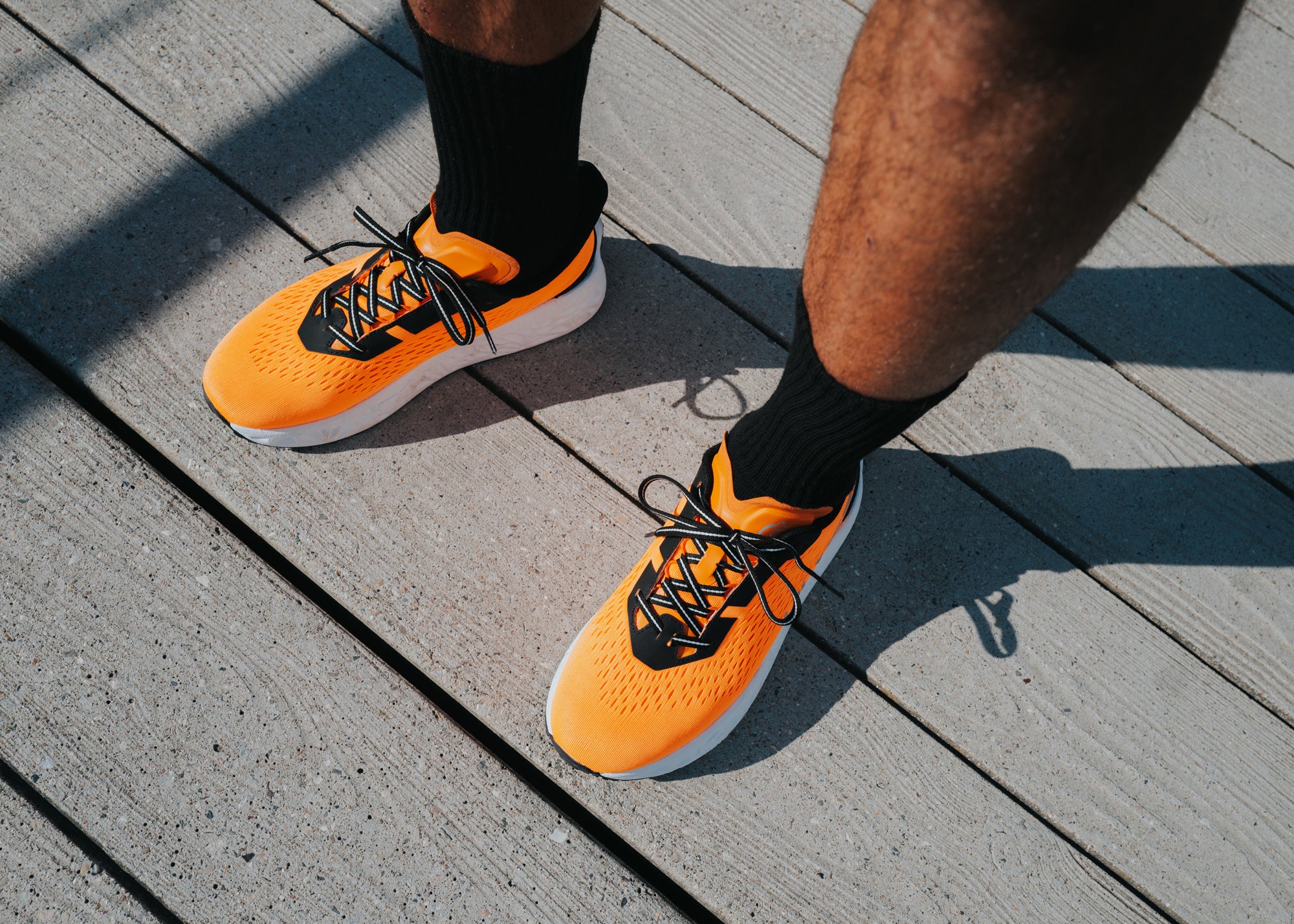 Close-up of a man's feet wearing orange and black Ulysses running shoes with black socks, standing on a wooden deck.